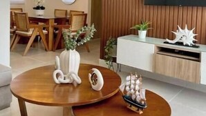 A modern living room with a wooden dining table, a TV mounted on a wooden panel wall, and a white console table with decorative items.
