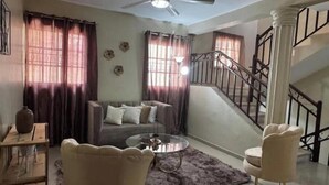 Una sala de estar con sofá, sillones, una mesa de centro y una escalera.
