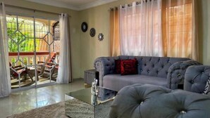 Una sala de estar con un sofá gris, una mesa de centro de vidrio y vistas a un balcón con mobiliario exterior.