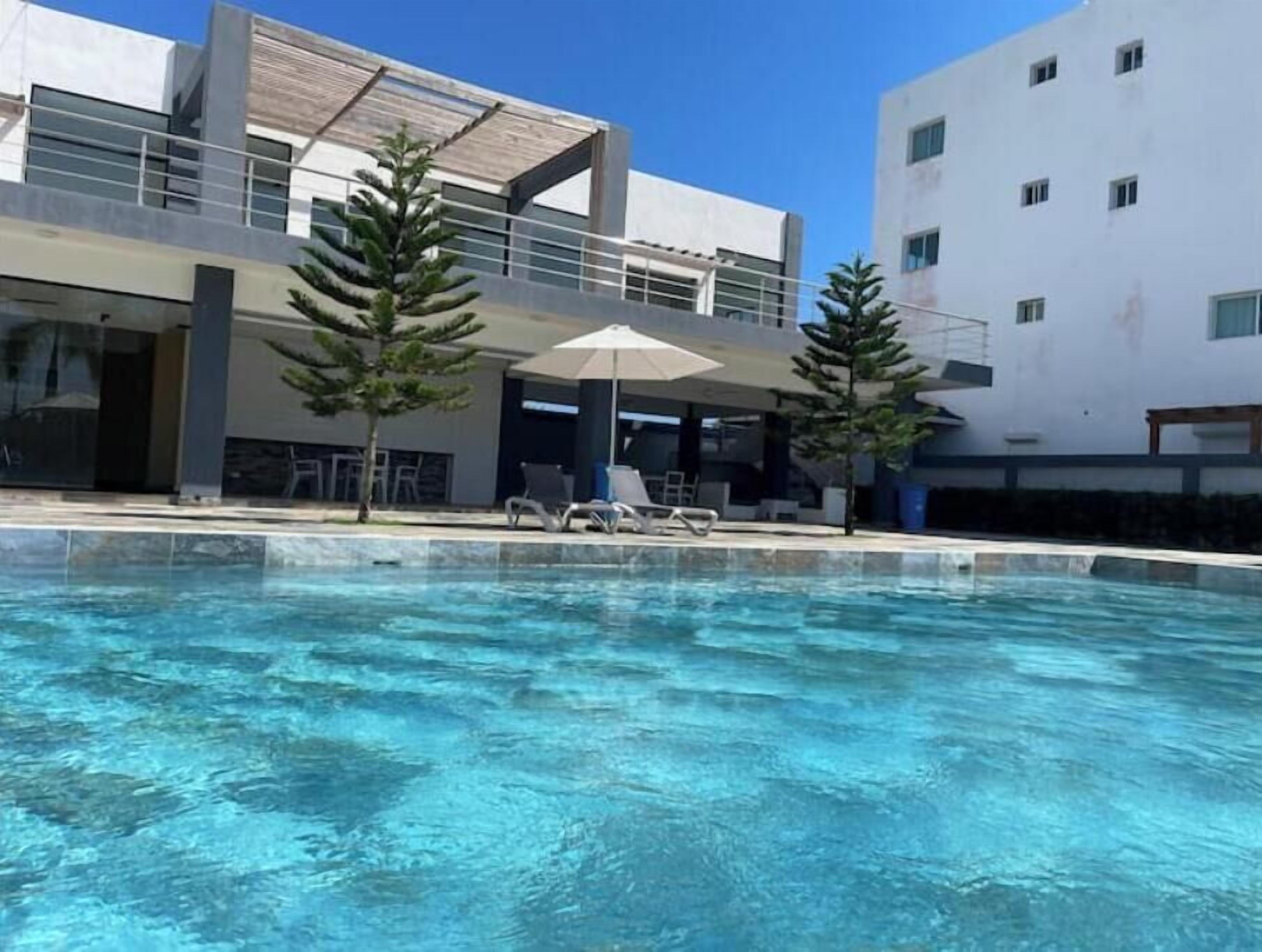 Ein modernes Gebäude mit Schwimmbad, Liegestühlen und Sonnenschirmen.
