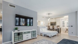 A modern bedroom with a bed, a TV mounted on the wall, a white bedside table, and a small plant.