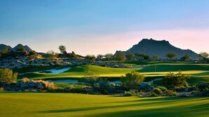 A golf course with a clear sky, green grass, and a mountain in the background.