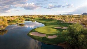 A golf course with a lake, sand bunkers, and a mountain in the background.