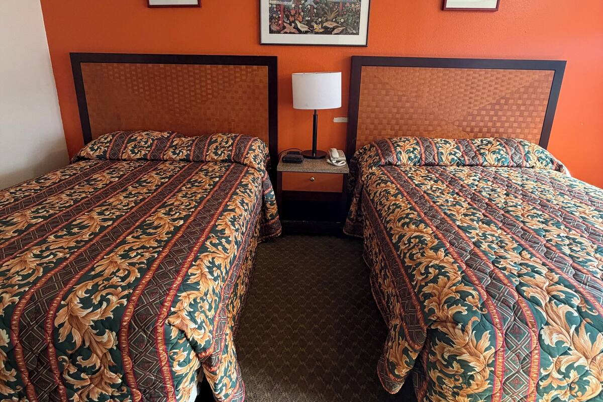 A hotel room with two beds, a nightstand with a lamp, and framed pictures on the wall.