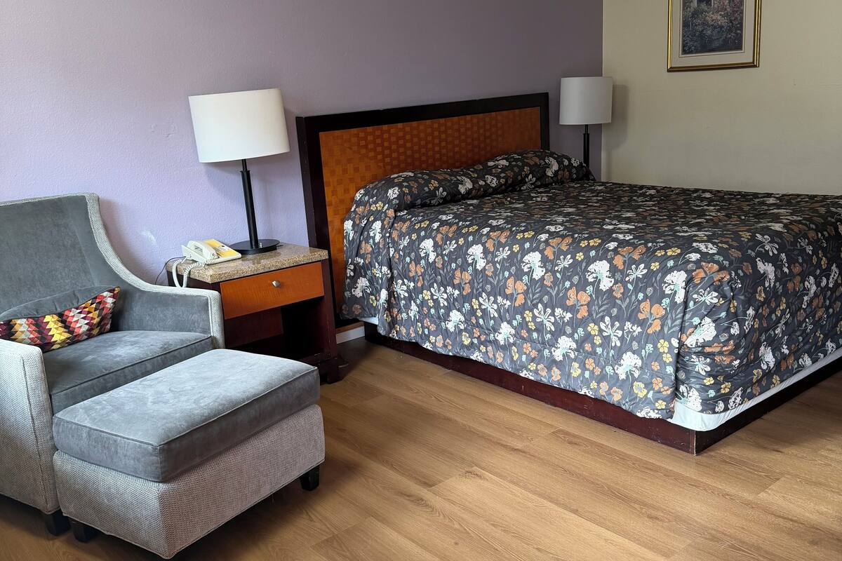 A hotel room with a bed, a sofa, a nightstand, and a lamp.