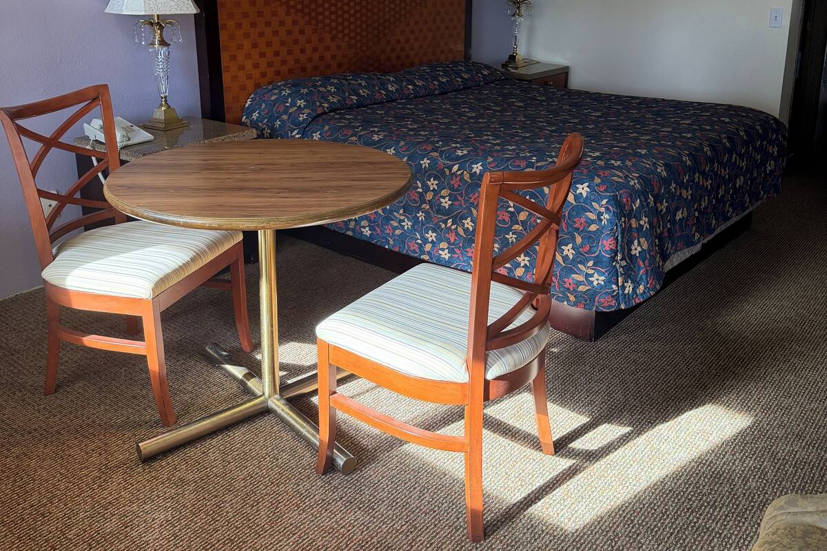 A hotel room with a bed, two chairs, a table, and three framed pictures on the wall.
