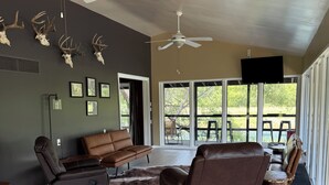 Ein geräumiges Wohnzimmer mit Deckenventilator, Ledersofas, einem großen Fenster mit Blick und aufgehängten Hirschskulpturen an der Wand.