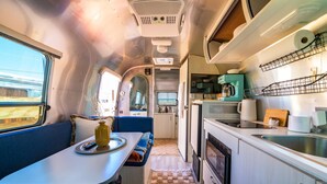 A compact kitchenette with a stove, sink, and a small refrigerator. There is a dining area with a table and bench, and a window providing natural light.
