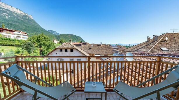 Un balcon avec deux fauteuils et une petite table, offrant une vue sur un paysage montagneux parsemé de bâtiments traditionnels.