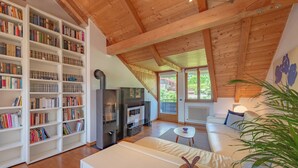 Un salon chaleureux avec une cheminée, des étagères à livres, un canapé et une vue sur l’extérieur.