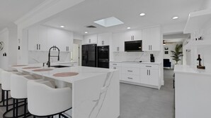 A modern kitchen with white cabinetry, a central island with bar stools, and built-in appliances.