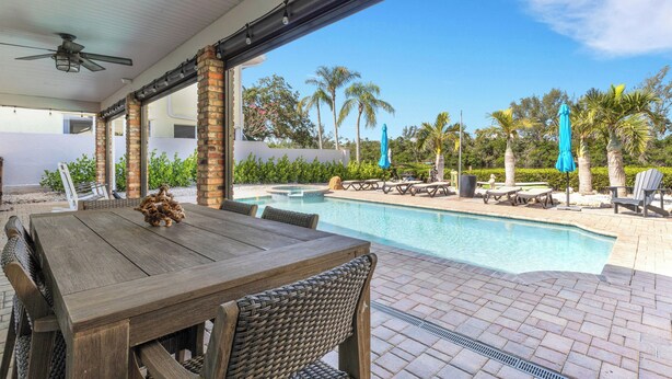 A covered outdoor area with a pool, wooden table, wicker chairs, and umbrellas.
