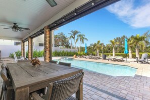 A covered outdoor area with a pool, wooden table, wicker chairs, and umbrellas. - Paradise in Siesta Key Poolside Vibes & Island Highs –You’ll Never Want to Leave (Sarasota)