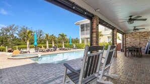 A poolside area with a brick patio, outdoor seating, and a view of a building with a balcony.