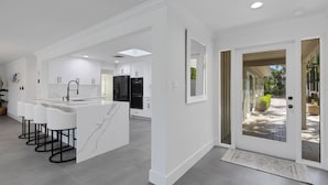 A modern kitchen with white cabinetry, a central island with bar stools, and a view through a glass door to an outdoor patio.
