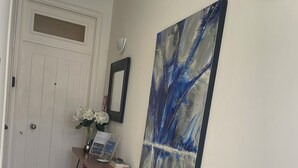 A hallway with a patterned floor, a door, a desk with a vase of flowers, and a large abstract painting on the wall. - Terrace bliss hot.Tub&city strolls ,5-10 m walk to restaurants and entertainment (Ponta Delgada)
