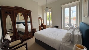 A bedroom with a large bed, a wooden wardrobe, a mirror, and a window with a view of buildings. - Terrace bliss hot.Tub&city strolls ,5-10 m walk to restaurants and entertainment (Ponta Delgada)