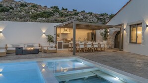 A modern outdoor pool area with a hot tub, seating, and a covered patio.