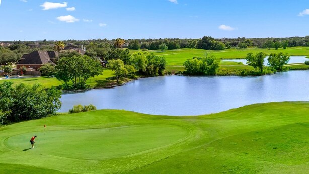 Un campo de golf con un cuerpo de agua, césped verde exuberante y casas residenciales al fondo.