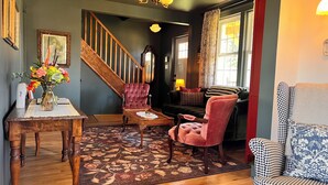 Una sala de estar con una escalera de madera, un tapete floral y un sofá con cojines estampados.
