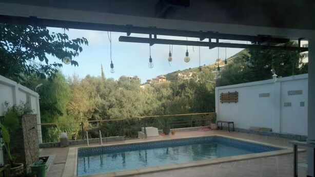 Une piscine extérieure dotée d’une terrasse carrelée, entourée de plantes en pot et d’une clôture blanche.