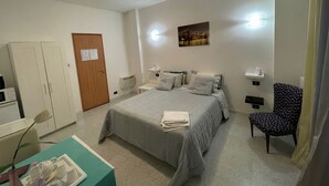Een hotelkamer met een bed, een bureau met een computer, een stoel en een foto aan de muur.