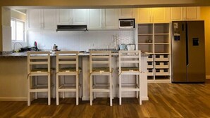 Una cucina con mobili bianchi, un forno a microonde, un frigorifero e un'isola in legno con sedie.