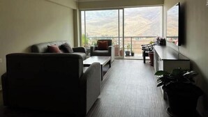 Un soggiorno moderno con divano, poltrona e tavolino. Un balcone offre vista sulle montagne.