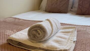 A neatly made bed with a rolled-up towel and a folded blanket on a textured pink bedspread.