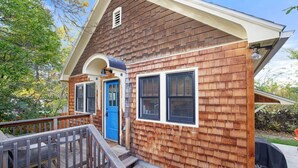 A wooden house with a porch, a blue door, and a small staircase leading to the entrance.
