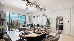 A modern dining area with a round table set for six, a city view through large windows, and a contemporary chandelier.