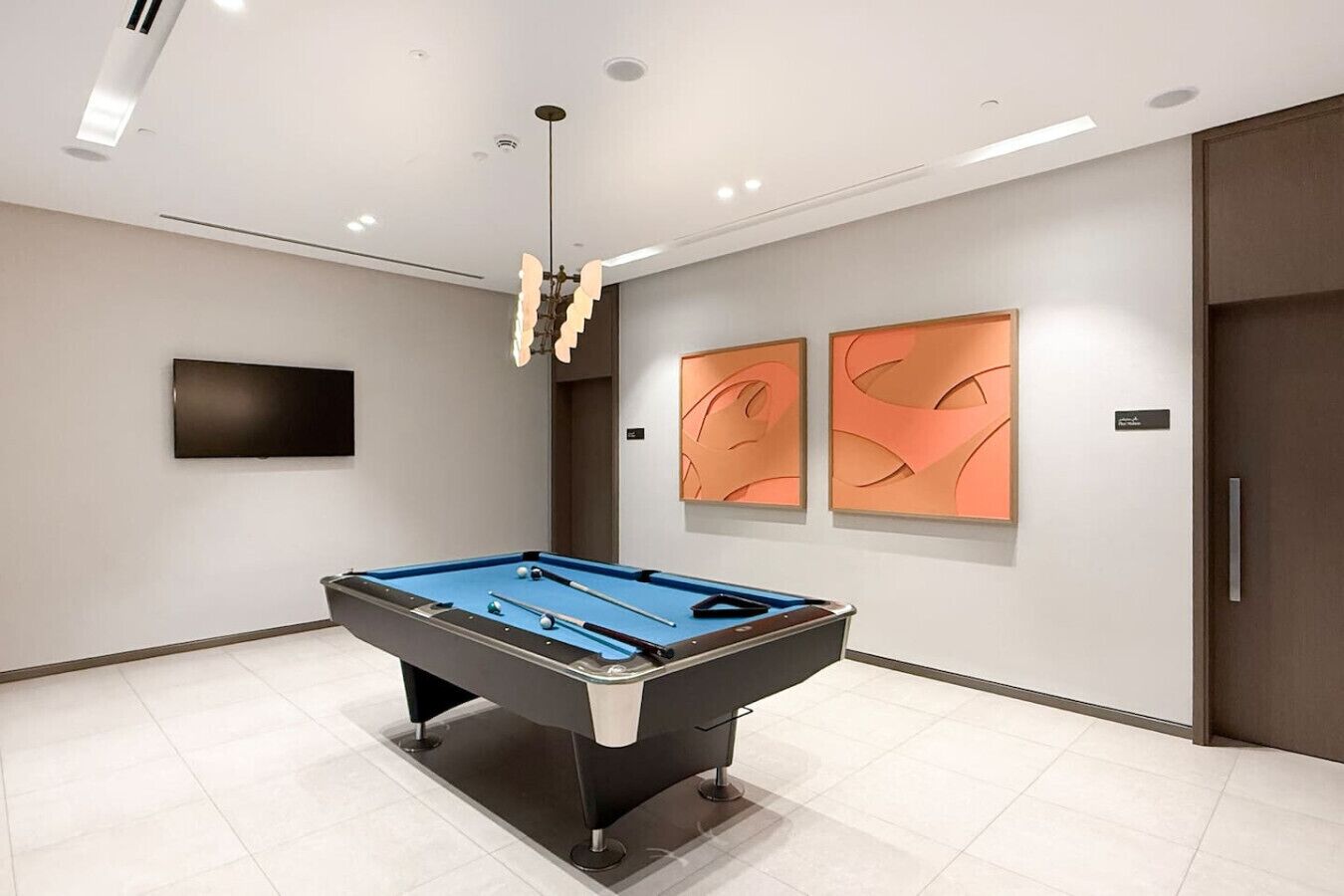 A pool table in a modern room with a flat-screen TV, abstract wall art, and a ceiling light fixture.