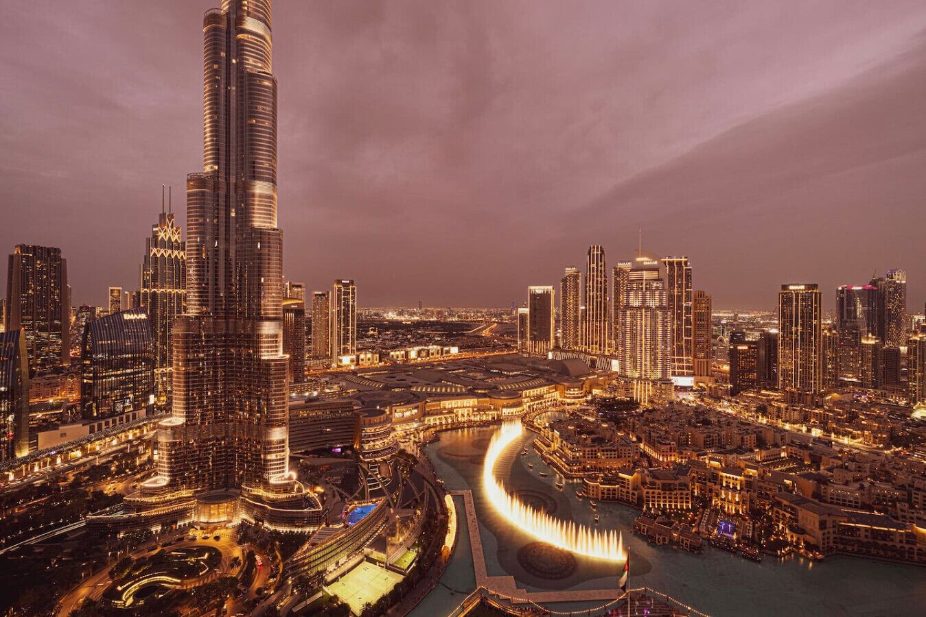 A cityscape at night with a prominent skyscraper, a waterfront area, and a curved road.