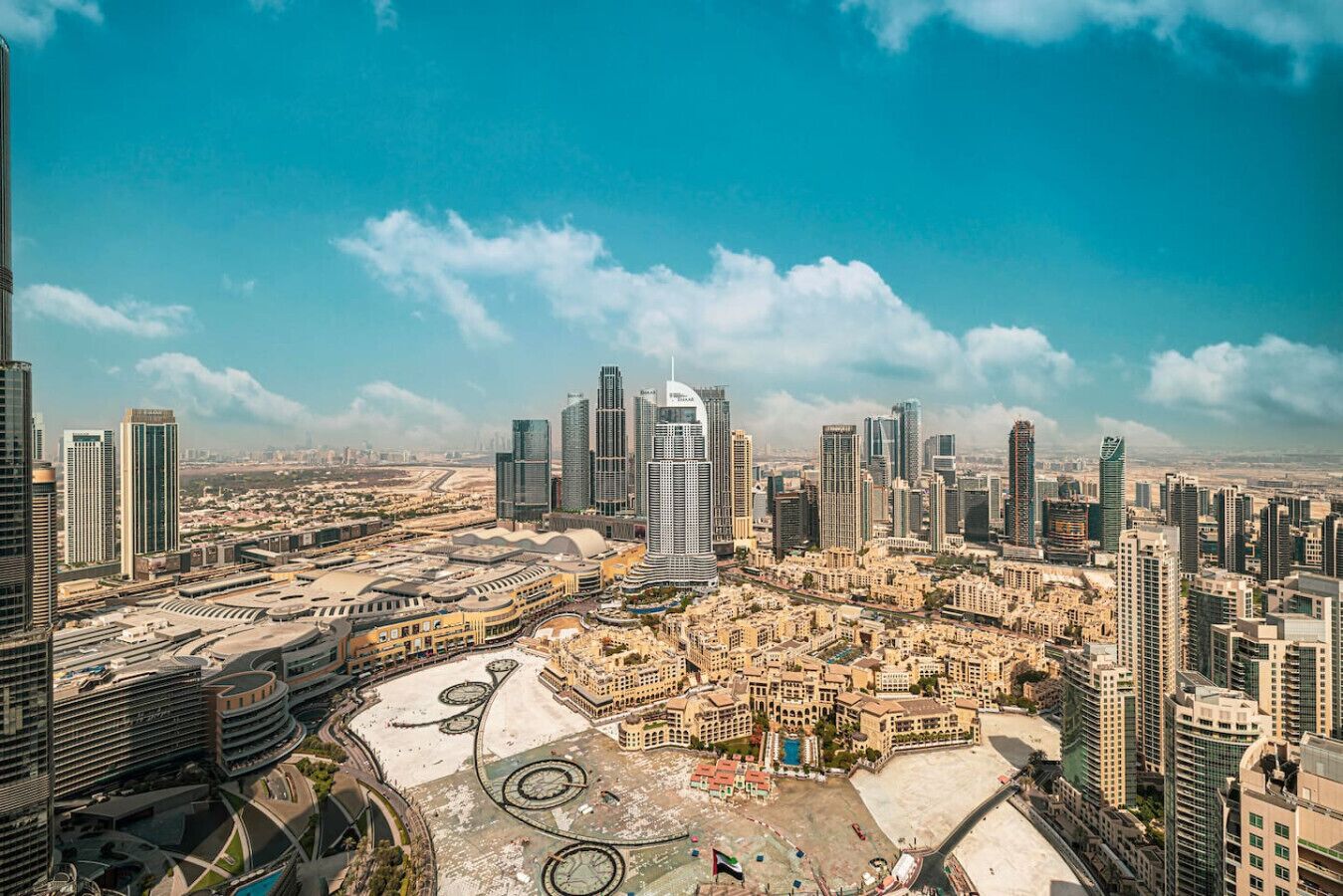 Un paysage urbain avec de modernes gratte-ciel, une vaste place centrale et un ciel bleu dégagé.