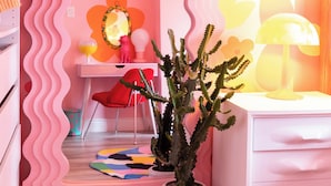 Una habitación con decoración rosa, un tocador, una planta de cactus y un espejo.