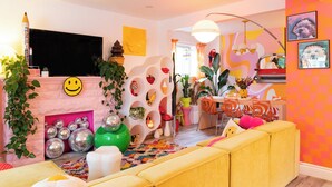 Un salón luminoso con un sofá amarillo, una chimenea con objetos decorativos, y un comedor con un modelo de coche rojo.