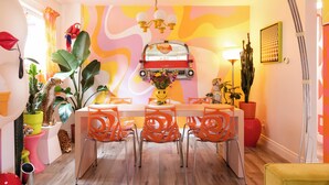 Comedor con una larga mesa, sillas naranjas y un mural en la pared.