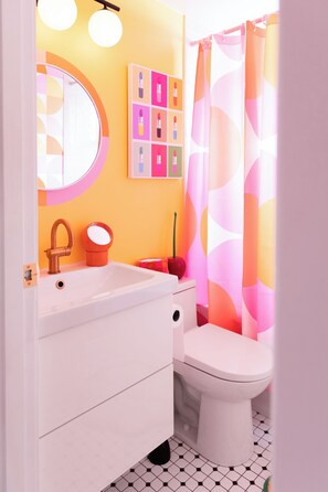 Une salle de bain avec un lavabo blanc, un miroir rond, des toilettes et un rideau de douche à motifs géométriques.