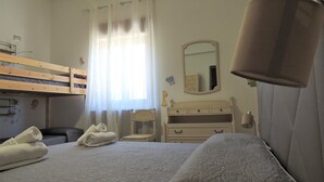 Un dormitorio con una cama litera, una mesita de noche, una silla, un aparador y un espejo.
