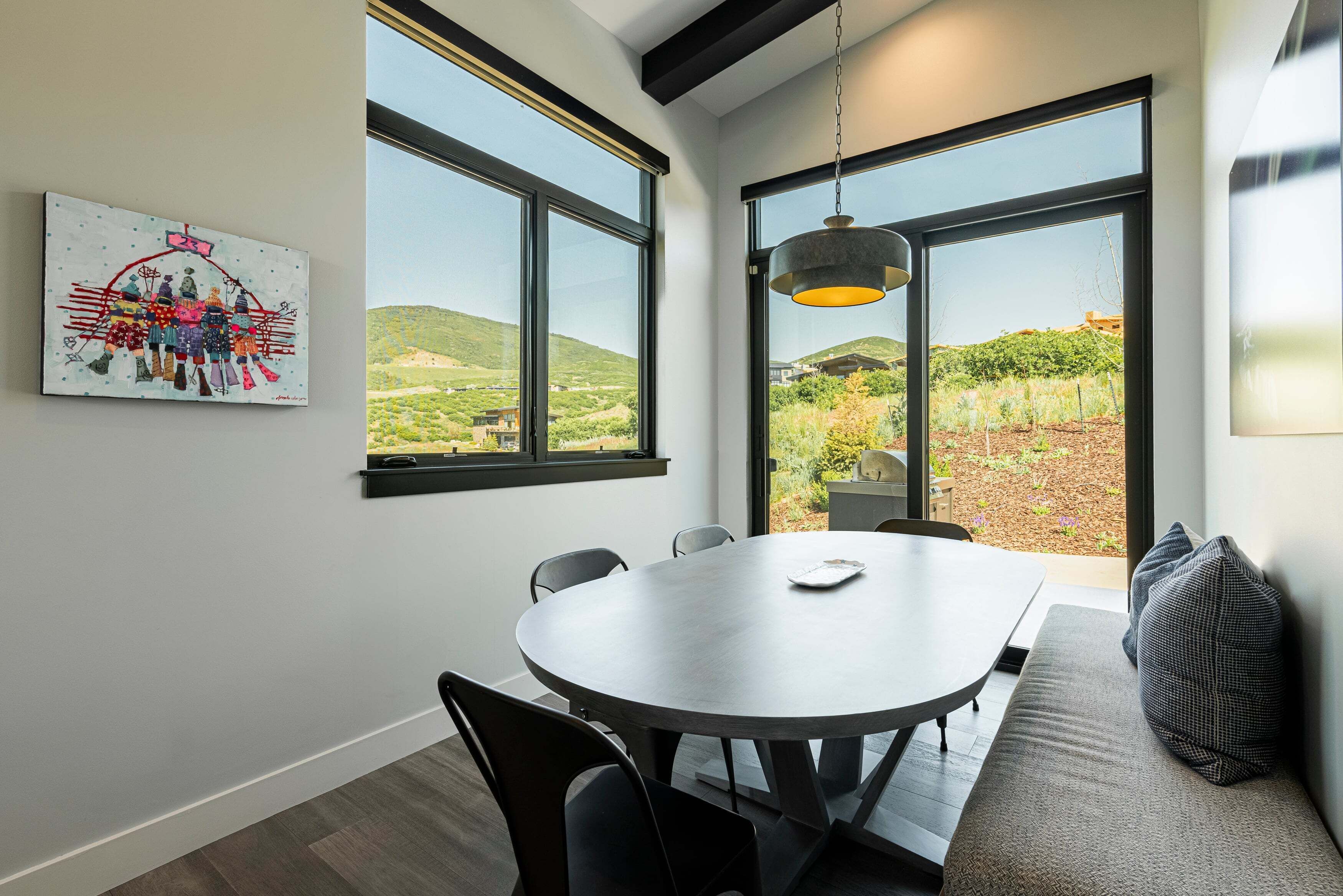 Un espace de repas moderne avec une table ronde, des chaises et un banc. De grandes fenêtres offrent une vue sur l’extérieur.
