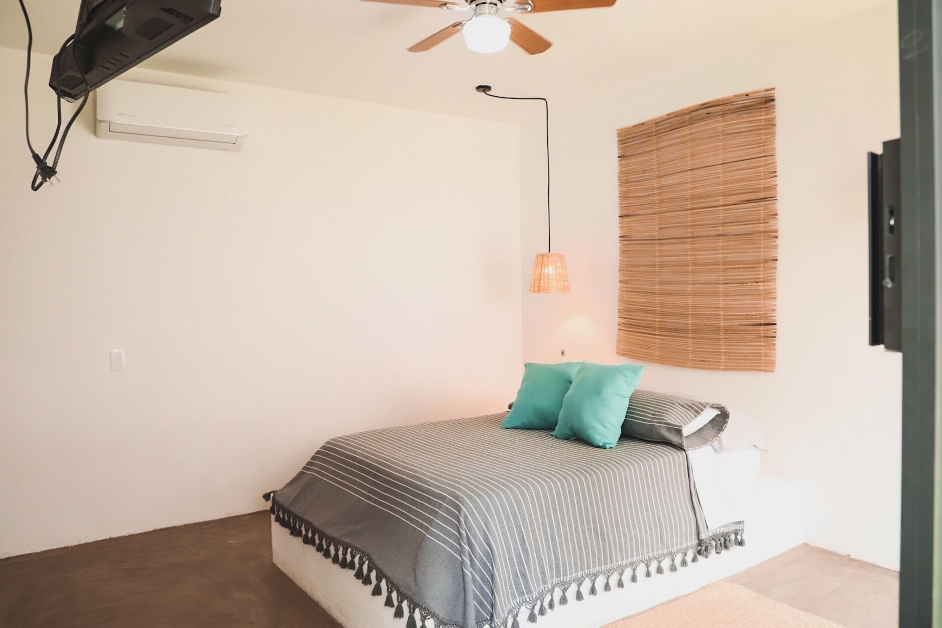 Un dormitorio con cama, ventilador de techo, aire acondicionado montado en la pared, lámpara colgante y ventana con persianas.