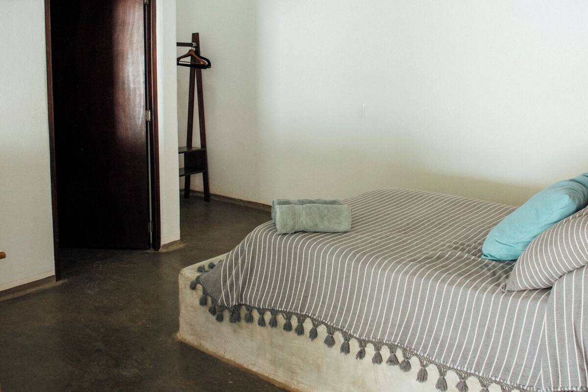 Un dormitorio con cama, ventilador de techo, lámpara colgante y una puerta que da a otra habitación.