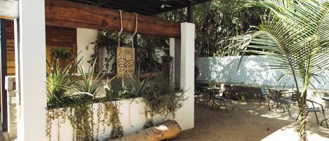 Un espacio de estar al aire libre con techo, plantas y un banco de madera.
