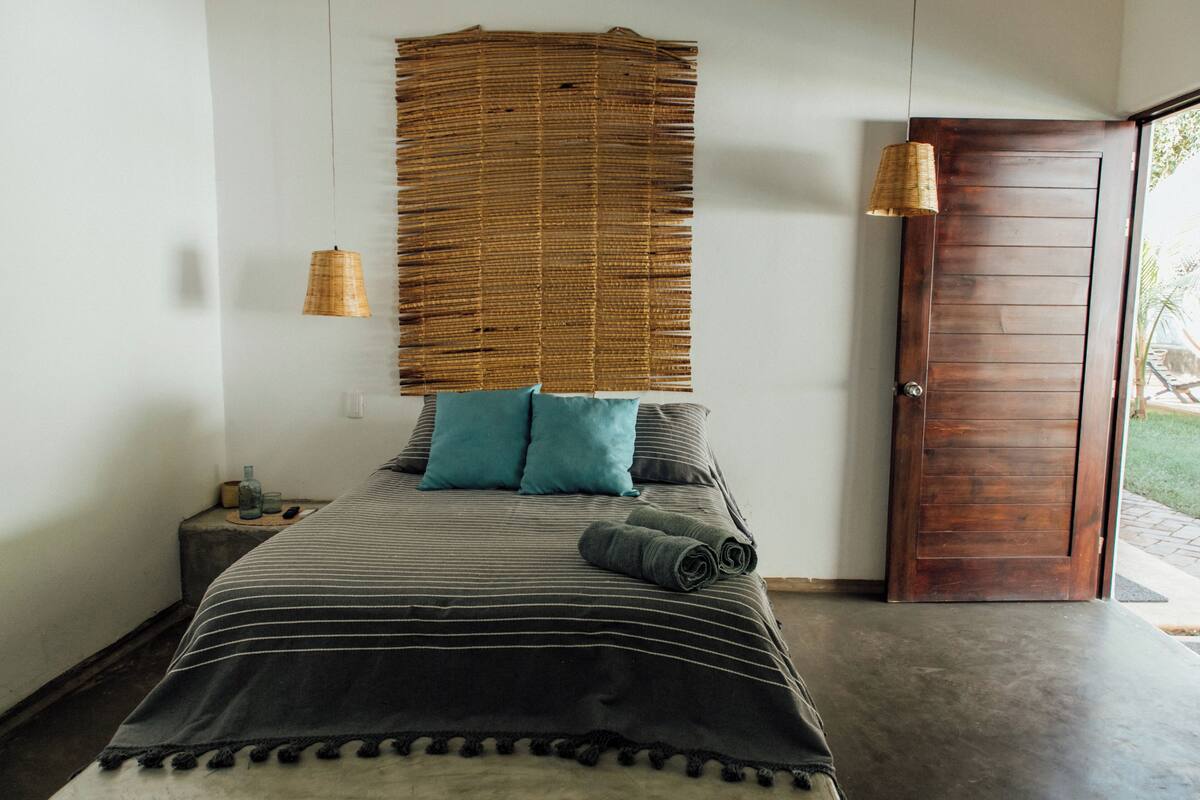 Un dormitorio con una cama, una mesita de noche, una lámpara y una puerta.