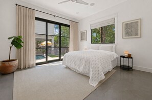 A bedroom with a large bed, a potted plant, and a view of a swimming pool.