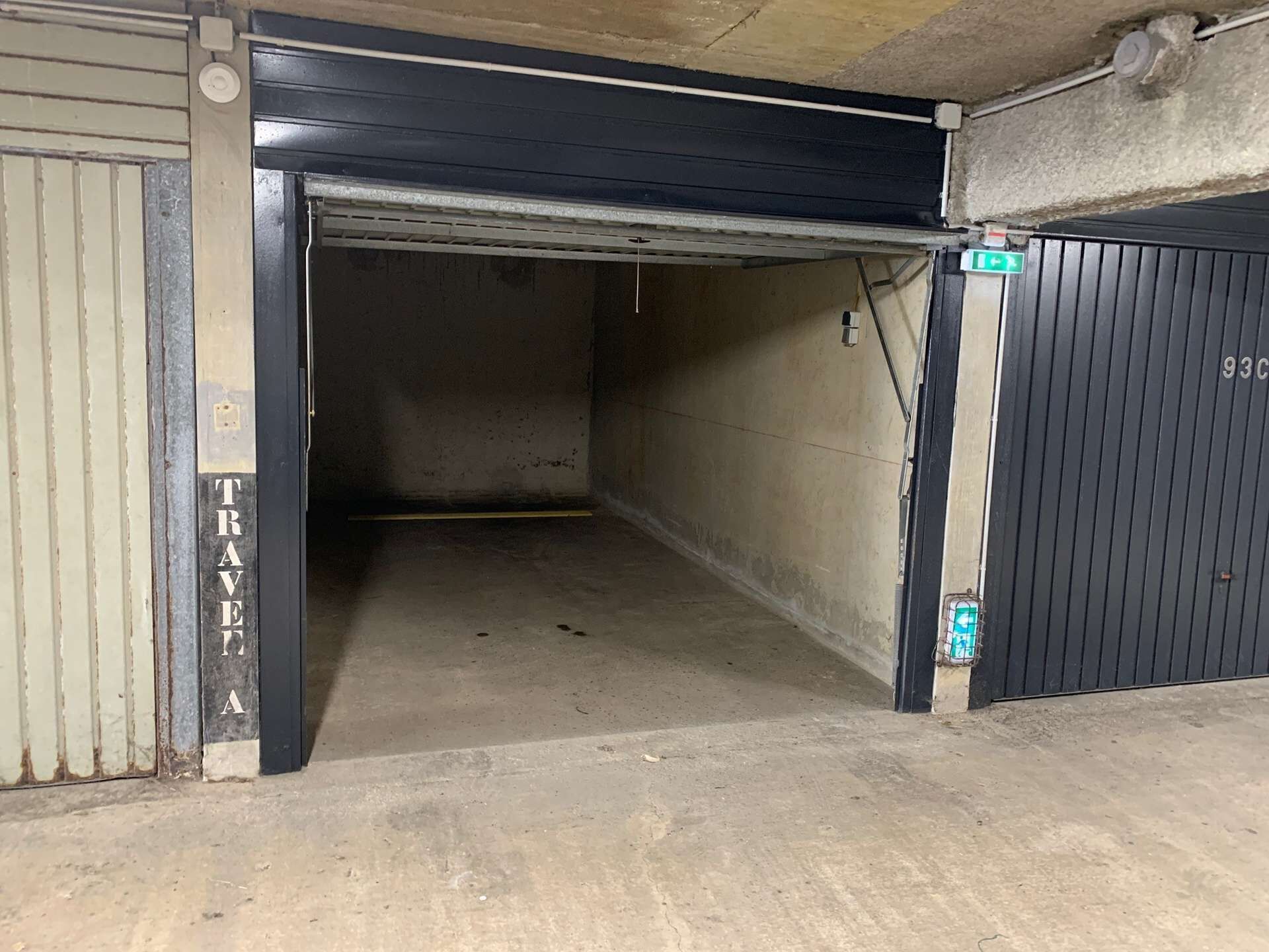 Een lege parkeergarage met een gesloten garagedeur aan de rechterkant en een deels open deur aan de linkerkant.