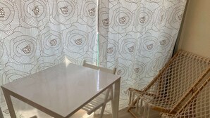 A room with a glass table, a macrame chair, and a patterned curtain. - Le Cocon de la corniche St Hilaire (SAINT HILAIRE DE RIEZ)