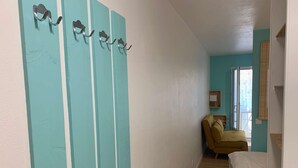 A narrow hallway with teal walls and a wooden floor, leading to a room with a bed and a window. - Le Cocon de la corniche St Hilaire (SAINT HILAIRE DE RIEZ)