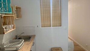 A kitchen with a wooden countertop, a sink, a window with blinds, and a small stool. - Le Cocon de la corniche St Hilaire (SAINT HILAIRE DE RIEZ)