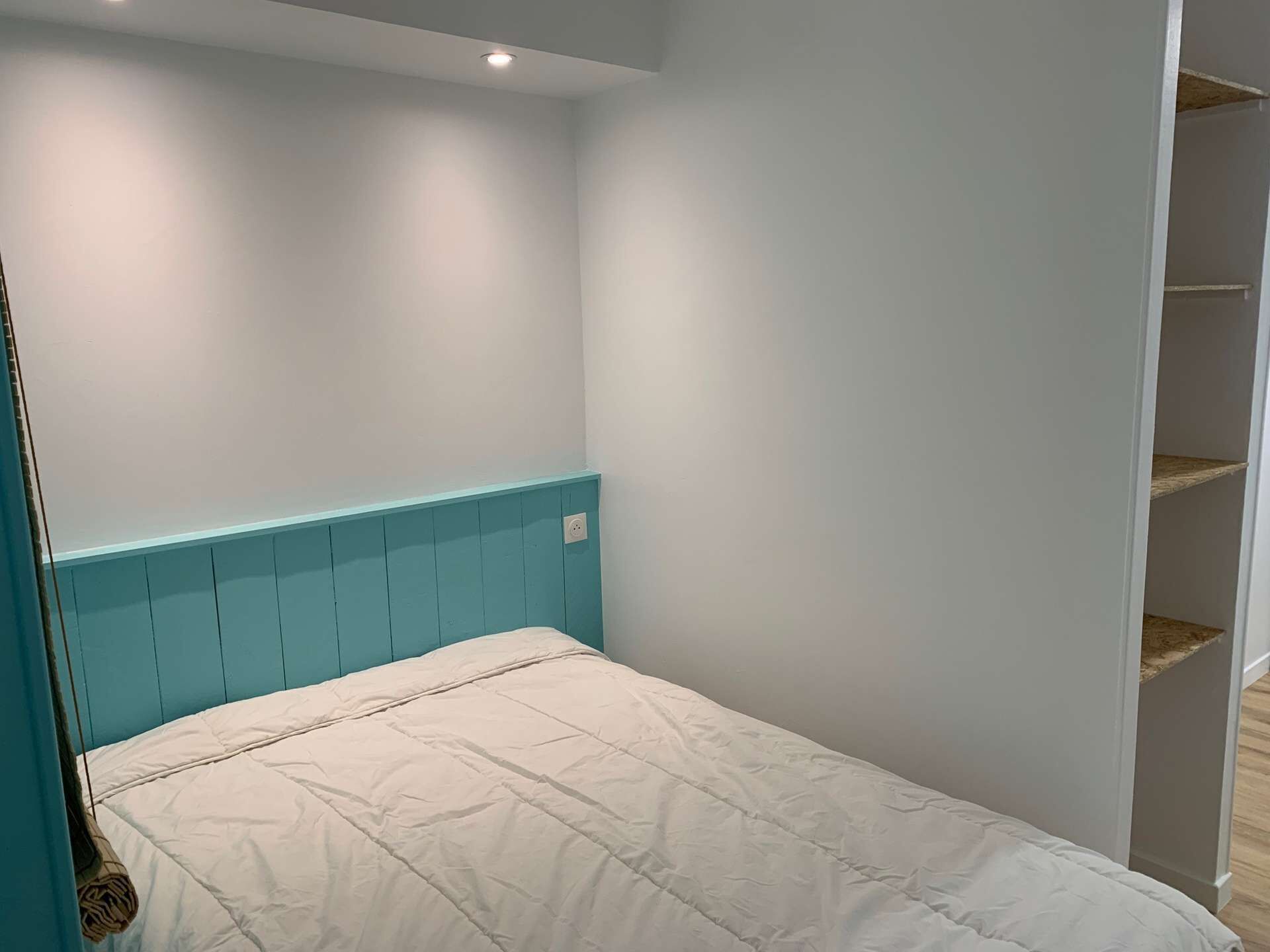 Ein Schlafzimmer mit einem Einzelbett, hellen Wänden und einem türkisblauen Kopfteil.